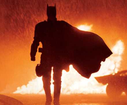 Robert Pattinson's Batman walks in front of fire in the rain in Matt Reeves' The Batman