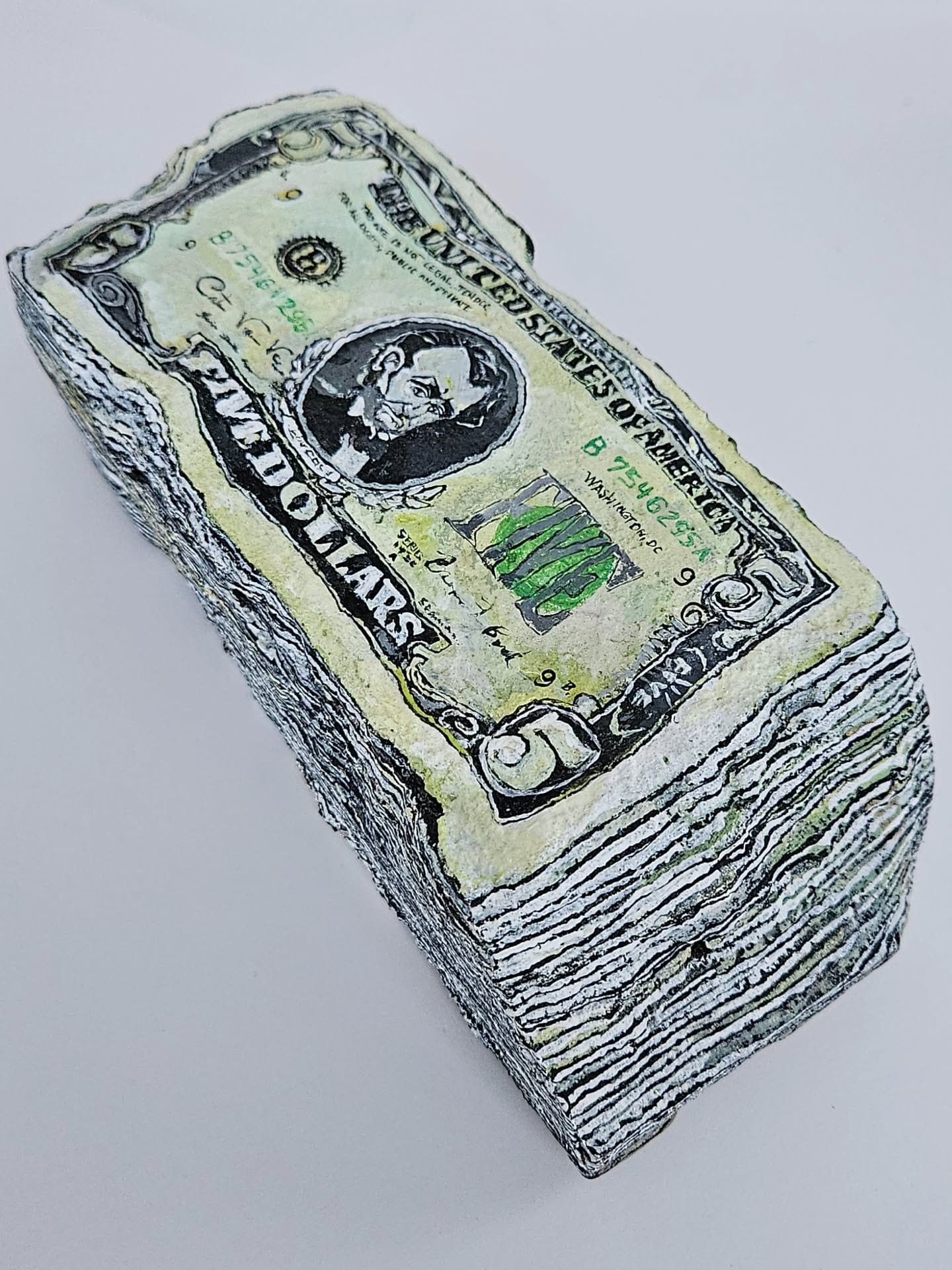 A painted rock sculpture by Elizabeth Saloka that resembles a stack of $5 bills