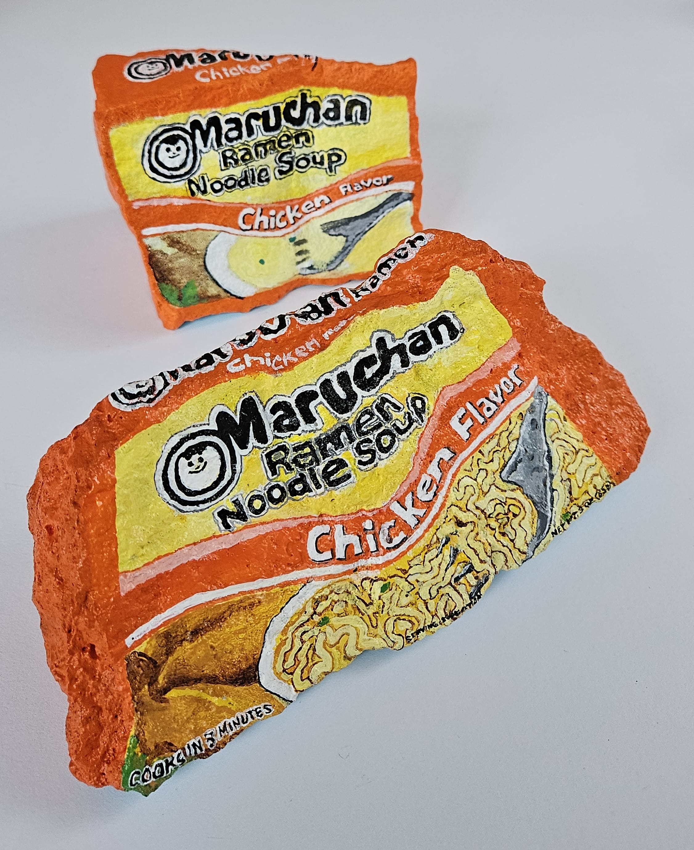 Two painted rocks by Elizabeth Saloka that resemble Maruchan brand chicken ramen packets