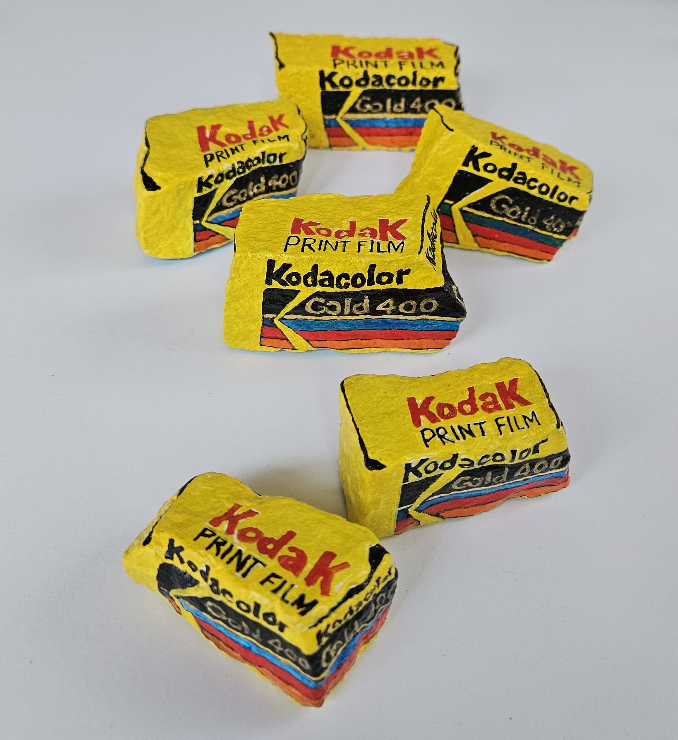 Painted rocks by Elizabeth Saloka that resemble six boxes of Kodak 35mm film