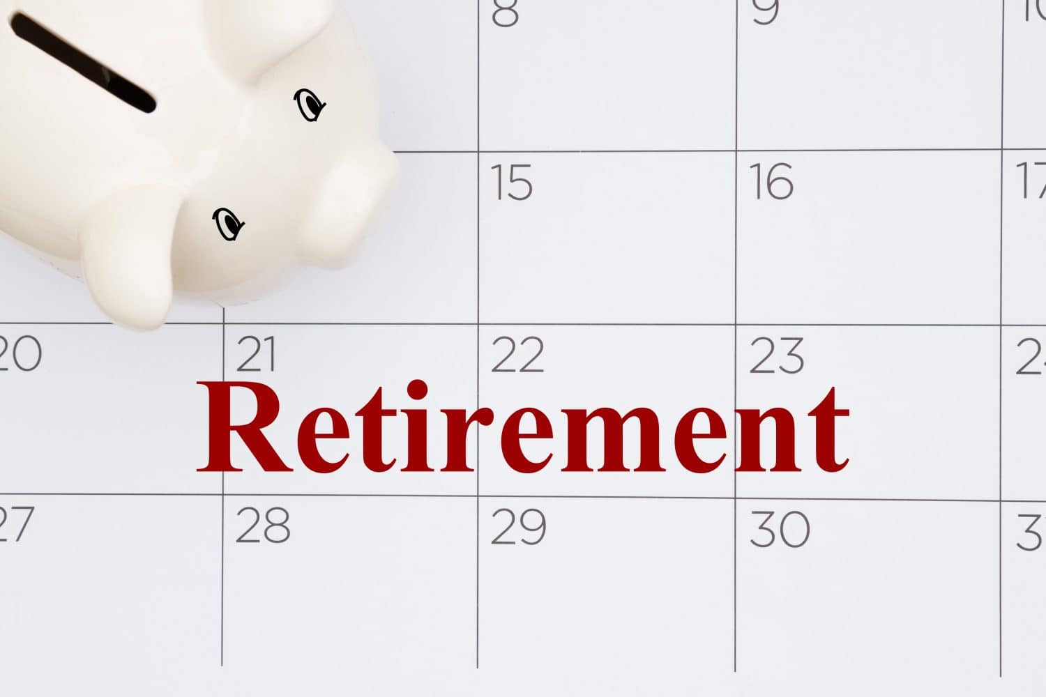 A white piggy bank sits on the top left corner of a white calendar. The word 'Retirement' is written in bold red letters across the center of the calendar, covering the dates for a few days in the third week of the month. Black numbers mark the other days on the calendar grid.