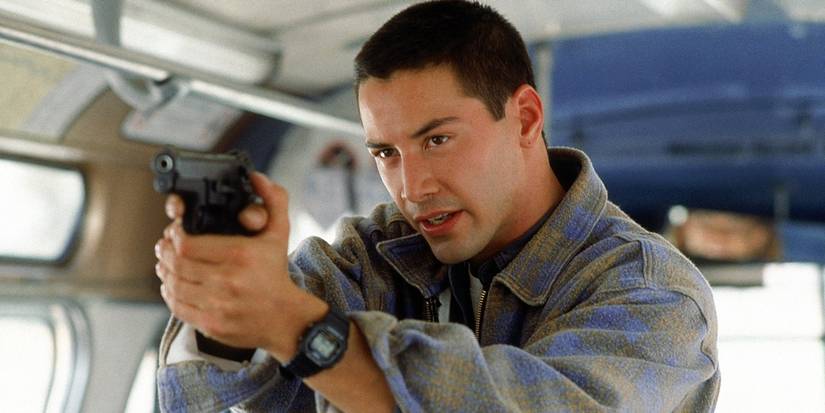Keanu Reeves as Jack on a bus, pointing a gun at a target offscreen, in Speed.