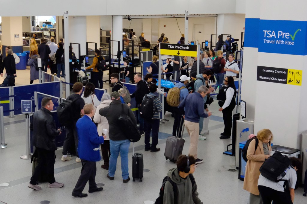 Travelers in line for security screening at Newark Liberty International Airport, with signs for TSA PreCheck, Economy Check-In, and Standard Checkpoint.