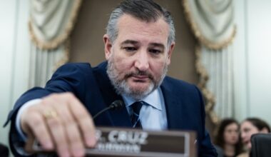 Senator Ted Cruz at a Senate committee hearing, sitting in his seat and using his hand to move a nameplate that says "Mr. Cruz, Chairman."