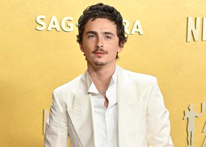 Timothée Chalamet in a white suit posing at the SAG Awards event against a gold background with SAG logo. Timothée Chalamet in a white suit posing at the SAG Awards event against a gold background with SAG logo.