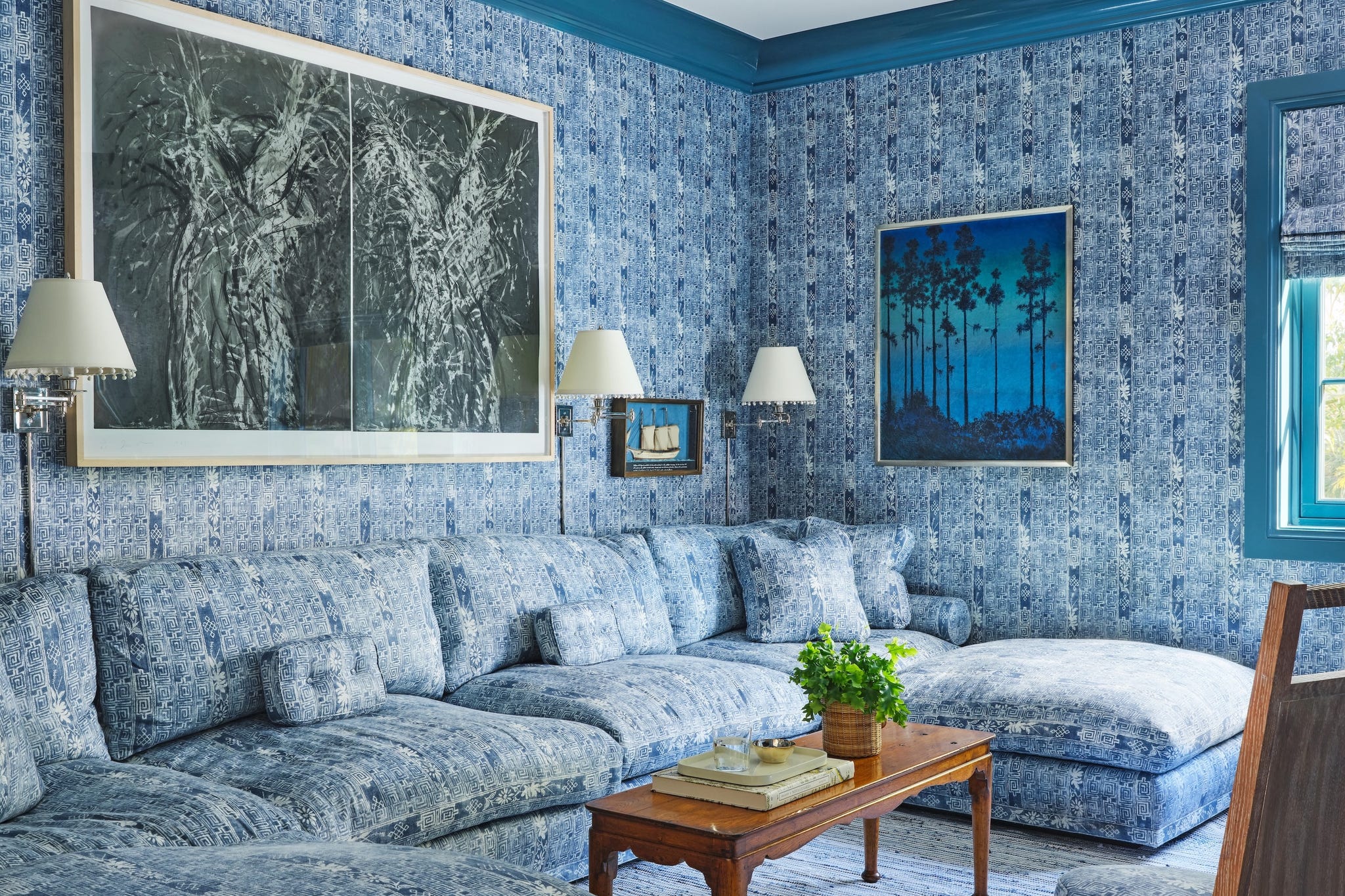 Living room with blue patterned walls and furniture, featuring modern art.