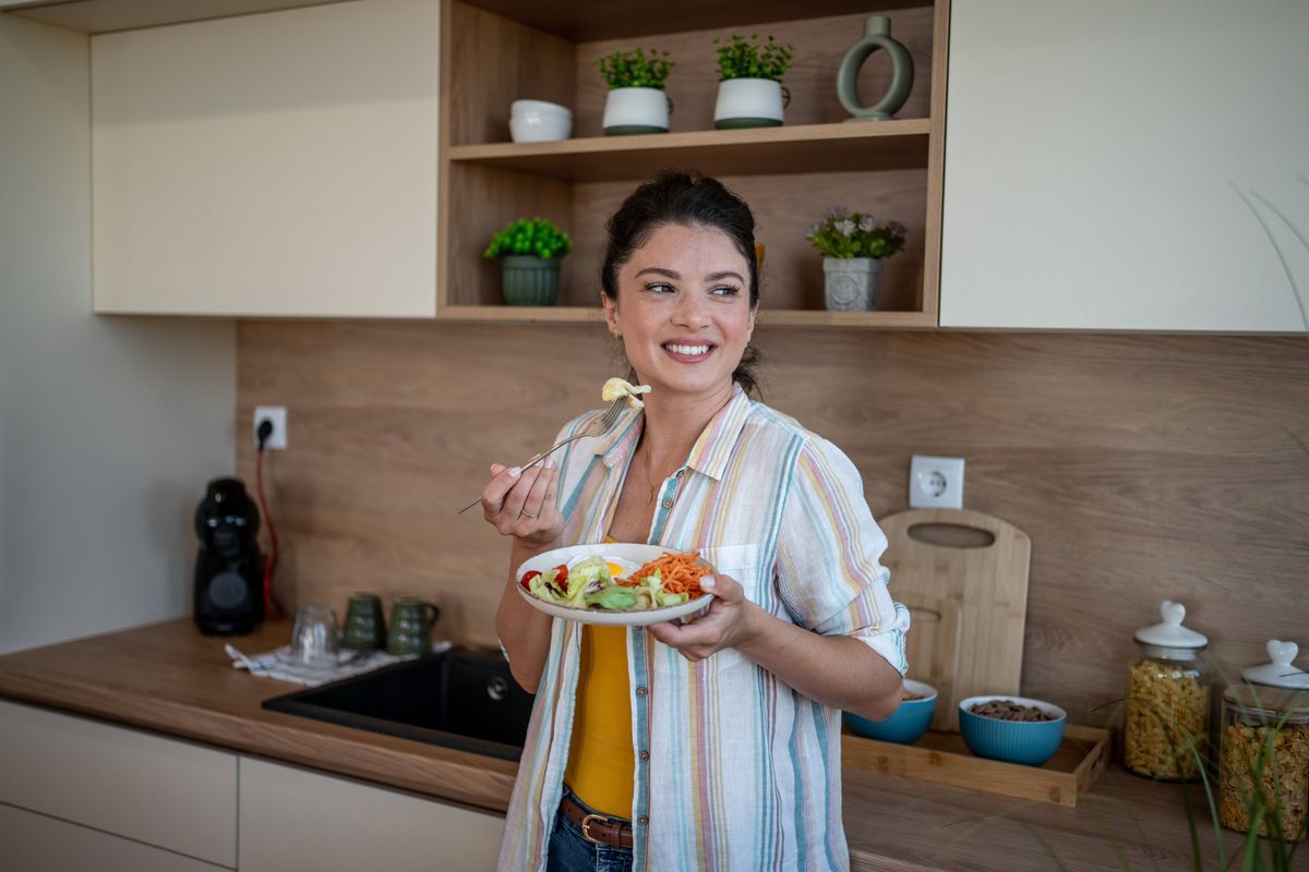 Cheerful woman enjoying a colorful and nutritious salad in a modern kitchen, celebrating a healthy lifestyle and savoring the flavors of fresh vegetables and wholesome ingredients