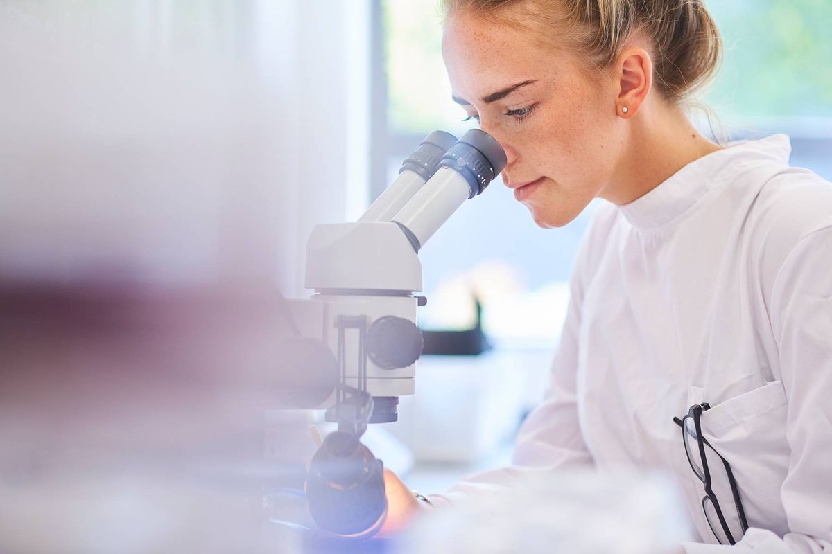 a female research scientist is analysing a sample on her microscope in a microbiology lab 