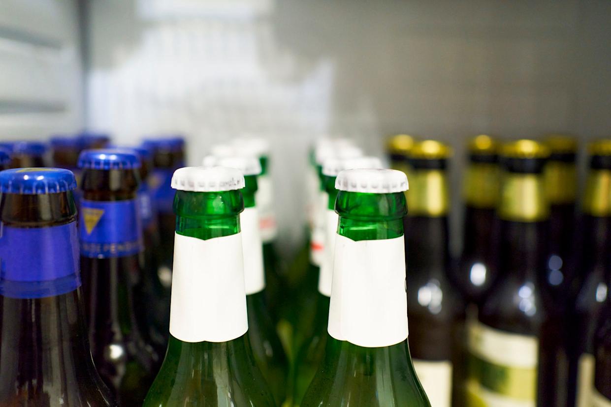 Close-up of beer bottles with white cap and beers with blue and gold details in the background inside the refrigerator