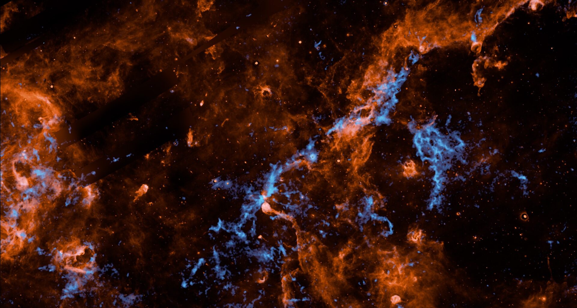 Wispy filaments of vibrant orange and electric blue cosmic dust and gas weave through a dark, star-studded expanse of outer space, creating a chaotic and intricate web of celestial matter.
