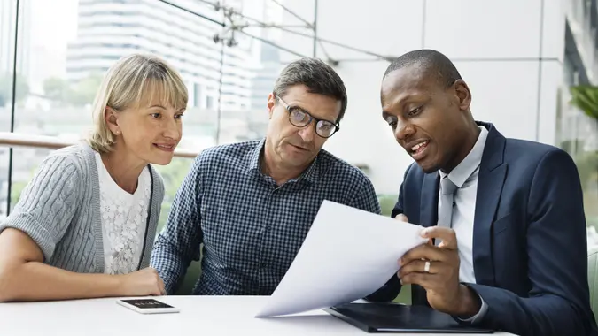A man and a woman look at a paper that another man is showing them.