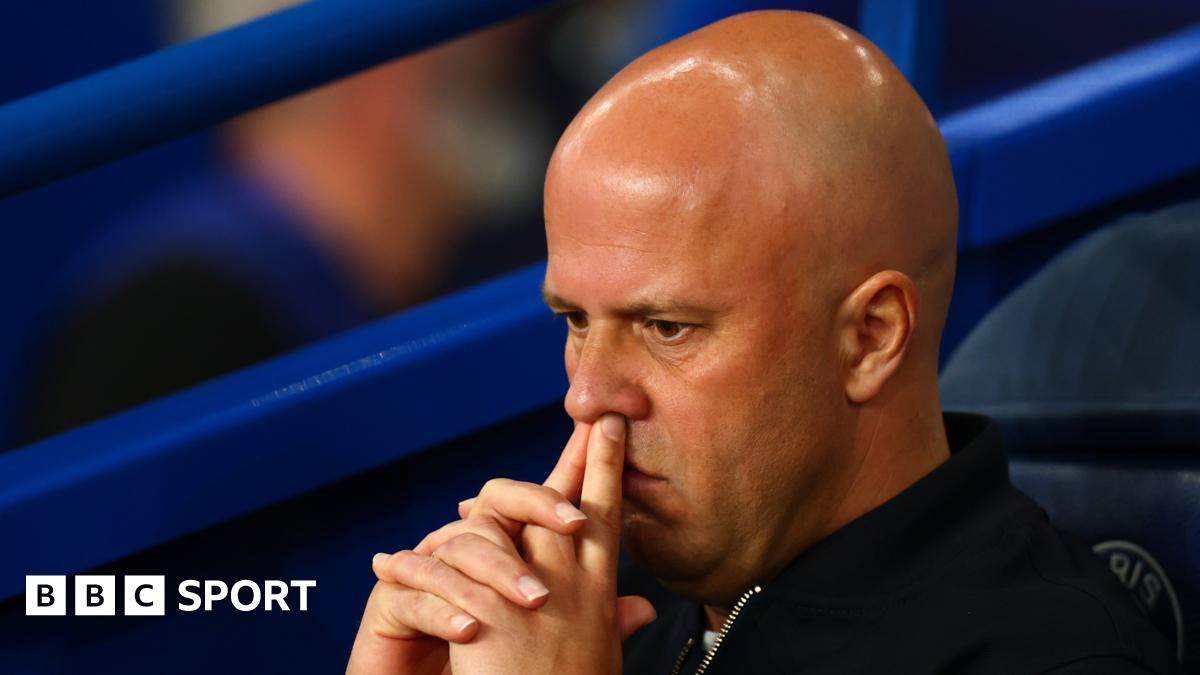 Headshot of Arne Slot, sitting on the bench, fingers on top lip, looking pensive