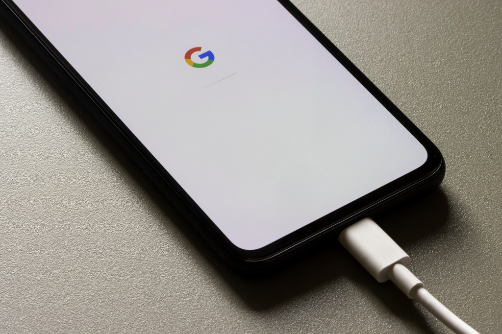 Google Pixel 4a smartphone with the Google logo and a progress bar displayed on its screen, connected to a white charging cable.