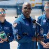 Artemis II crew members — mission specialist Christina Koch (left) and commander Reid Wiseman (right) — listen as pilot Victor Glover speaks to the media after arriving at the Kennedy Space Center on March 27, 2026 in Cape Canaveral, Florida. The astronauts' planned 10-day mission will take them around the Moon and back to Earth.