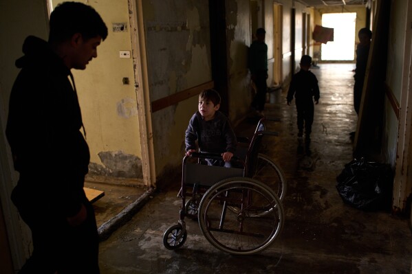 Abbas, 5, who suffers from a genetic condition that prevents him from walking, speaks with his father in a hallway of a hospital converted into a shelter in Beirut, Lebanon, Friday, March 27, 2026, after they were displaced from Dahiyeh, Beirut's southern suburbs. (AP Photo/Emilio Morenatti)