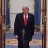 President Trump stands between two flags in the Cross Hall of the White House.