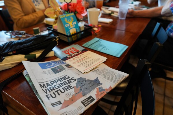 A print edition of the Goochland Gazette, with a front page story on the Virginia redistricting referendum, lies on a table at GG's Pizza as members of the Goochland Democratic Committee Jen Strozier, Doug Mock, Chris Svoboda, Richard Grebe and Judi Sheppard hold a lunch meeting on future get-out-the-vote efforts, Thursday, April 2, 2026, in Maiden, Va. (AP Photo/Julia Demaree Nikhinson)
