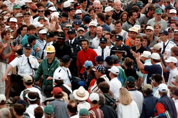 Masters champion Tiger Woods is engulfed by the gallery as he makes his way to the the 18th hole during final round play on April 13, 1997, at the Augusta National Golf Club in Augusta, Ga. (AP Photo/Amy Sancetta, File)