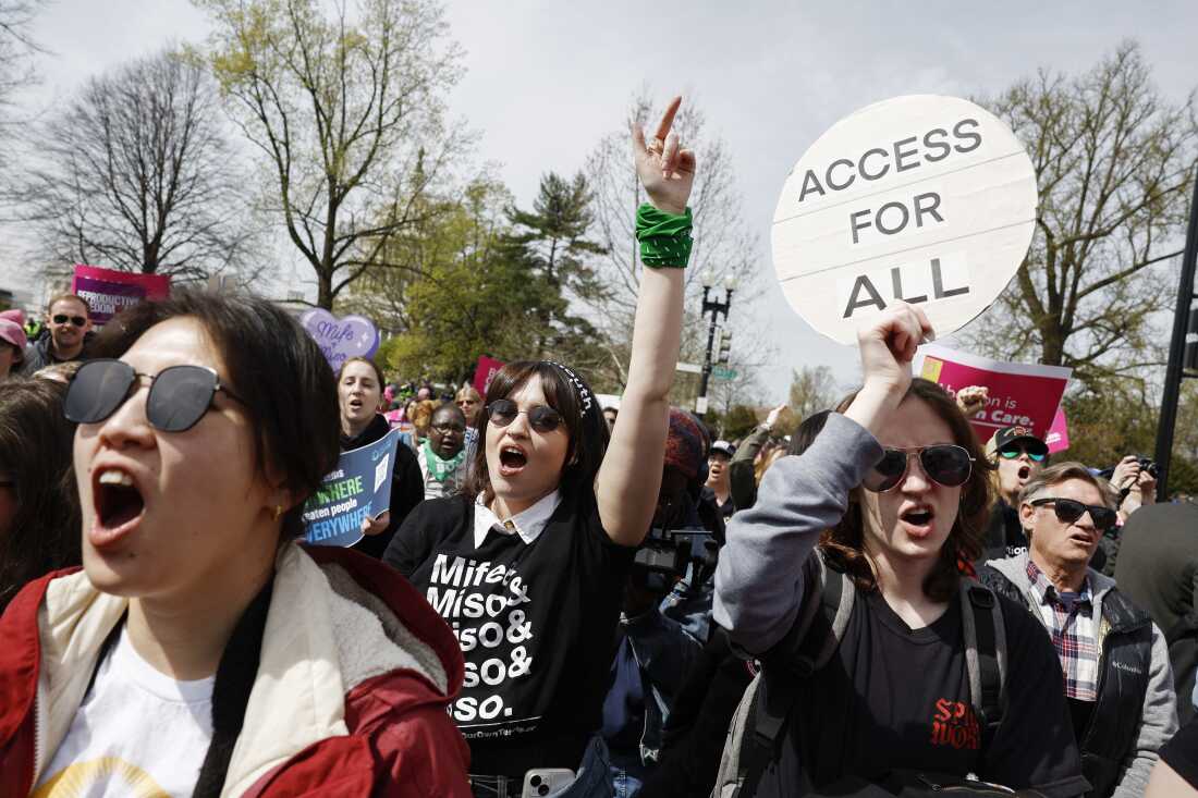 An abortion-rights rally shows young women shouting. One holds a sign that says "Access for All." Another wears a t-shirt that says, "Mife & Miso & Miso & Miso & Miso," a reference to the combination and doses of mifepristone and misoprostol drugs needed for a medication abortion.