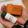 A person holds two packages of medicine in their hands, one in an orange box, the other in a white plastic pill bottle. In the background is an instruction sheet, with the headline "How to take your medication" partially visible.