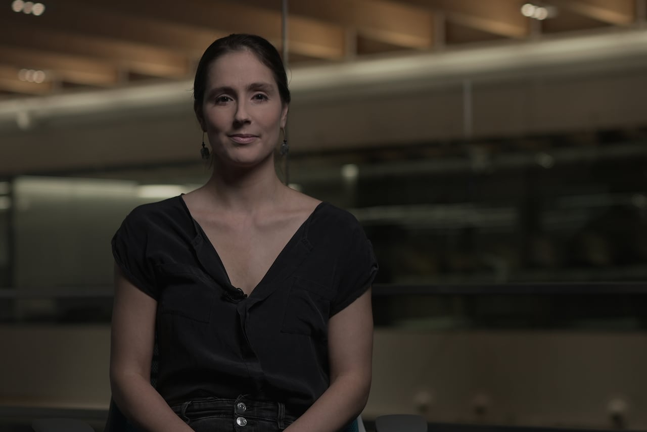 A woman sitting in a chair looks directly ahead.