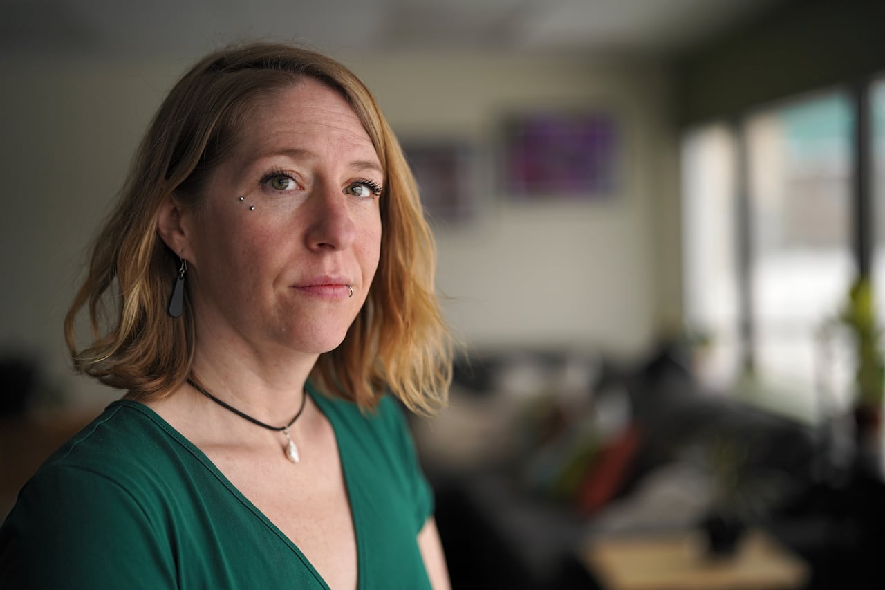 A woman looks at the camera, standing in front of a window