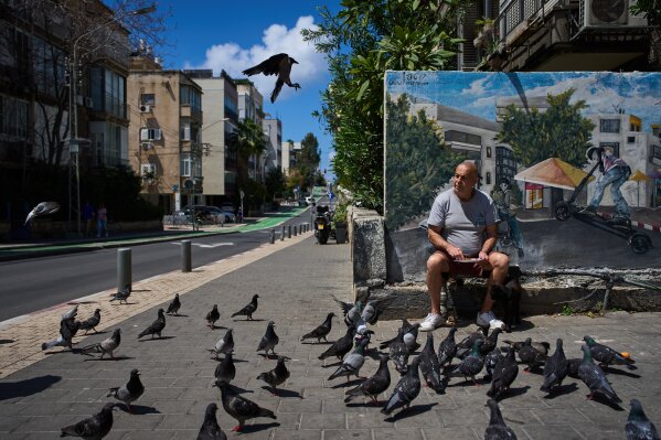 A man feeds birds on a street in Tel Aviv, Israel, after the announcement of a two-week ceasefire with Iran, Wednesday, April 8, 2026. (AP Photo/Oded Balilty, File)