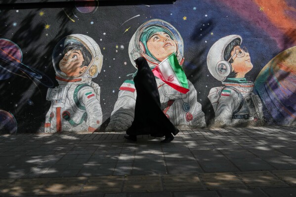 A woman walks past a mural in Tehran, Iran, Wednesday, April 8, 2026. (AP Photo/Francisco Seco, File)