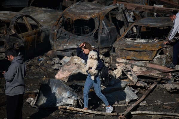 A woman holds her dog as she walks past burned cars a day after an Israeli airstrike in Beirut, Lebanon, Thursday, April 9, 2026. (AP Photo/Emilio Morenatti, File)