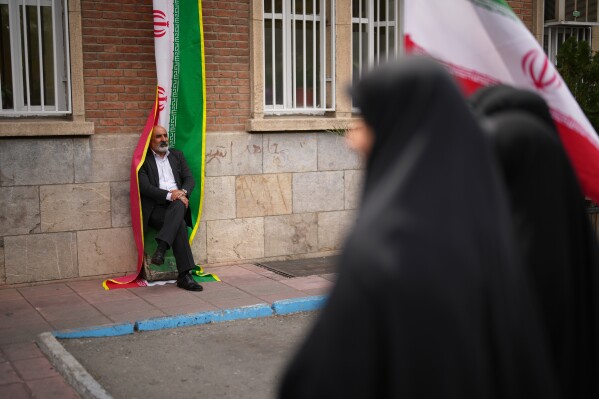A man leans against an Iranian flag banner during a government-sponsored protest attended by medical workers against the U.S.-Israeli military campaign outside Imam Khomeini Hospital in Tehran, Iran, Monday, April 6, 2026. (AP Photo/Francisco Seco, File)