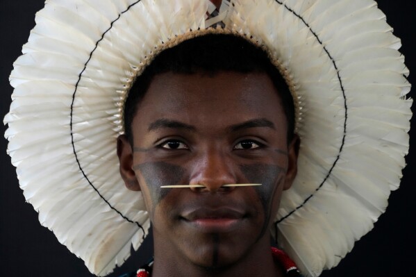 An Indigenous man wearing traditional face paint, feather headdress and piercing poses for a portrait during the opening of the "Acampamento Terra Livre," or Free Land Encampment, Brazil's largest annual Indigenous mobilization that focuses on land rights and environmental protection, in Brasilia, Brazil, Monday, April 6, 2026. (AP Photo/Eraldo Peres, File)