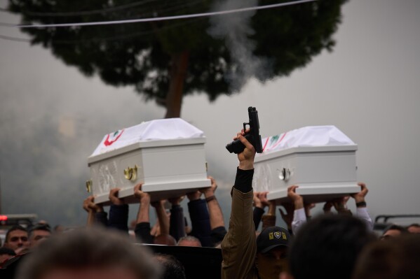 A gunman fires his gun as men carry the coffins with the bodies of Pierre Mouawad, an official with the anti-Hezbollah Lebanese Forces party, and his wife during their funeral in Yahshush, in Lebanon, Tuesday, April 7, 2026. (AP Photo/Emilio Morenatti, File)