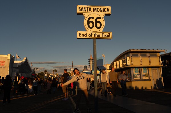 A visitor poses for photos with the "End of the Trail" Route 66 sign on the Santa Monica Pier in Santa Monica, Calif., Saturday, Nov. 22, 2025. (AP Photo/Jae C. Hong, File)