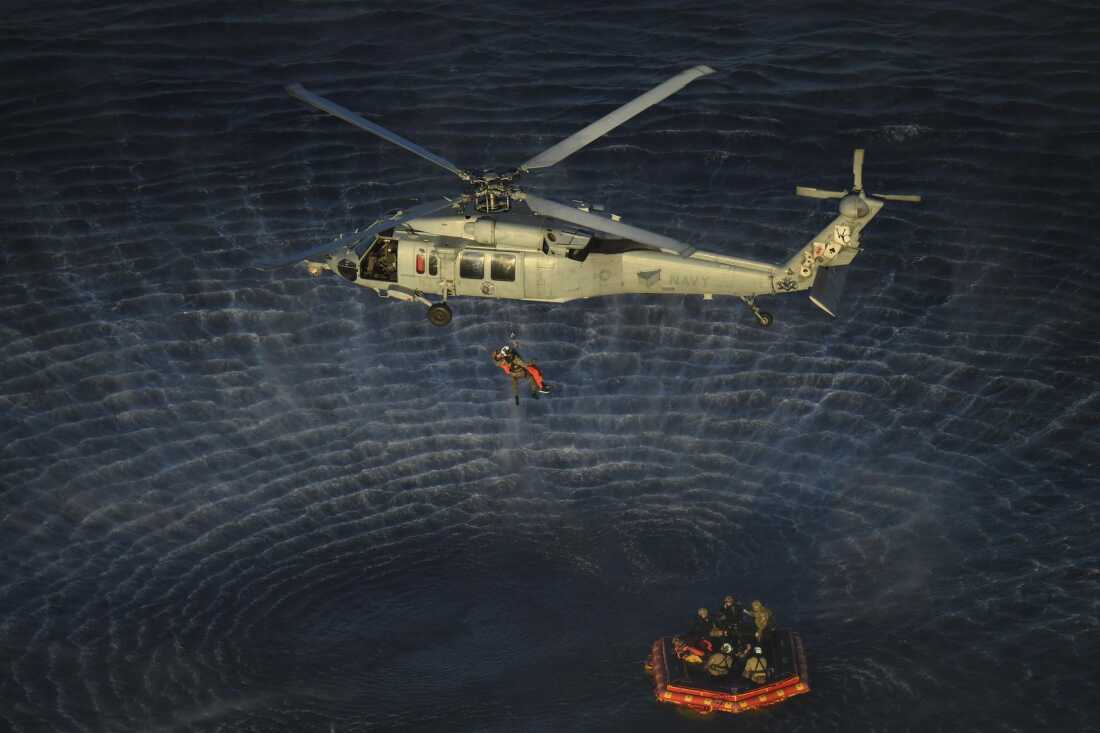 U.S. Navy divers and Artemis II astronauts aboard an inflatable raft are approached by helicopters and lifted away to the recovery ship.