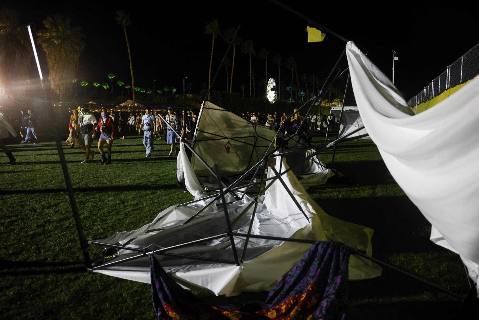 Festivalgoers walk past tents blown down by the wind at night.
