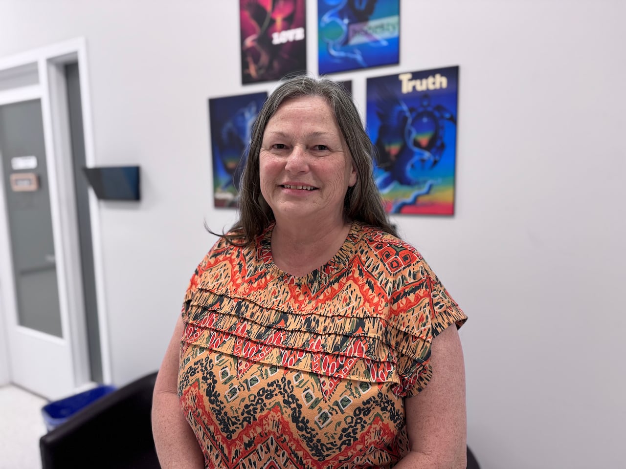 woman in patterned blouse seated near wall with posters