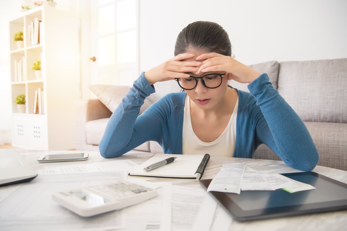 A person holds their head in woe as they look at the bills they need to pay.