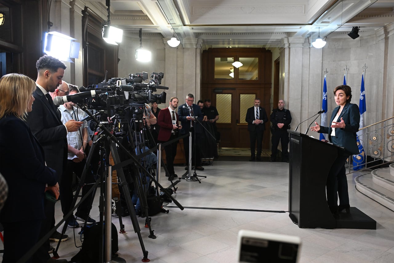wide shot of woman at podium with reporters and cameras on her