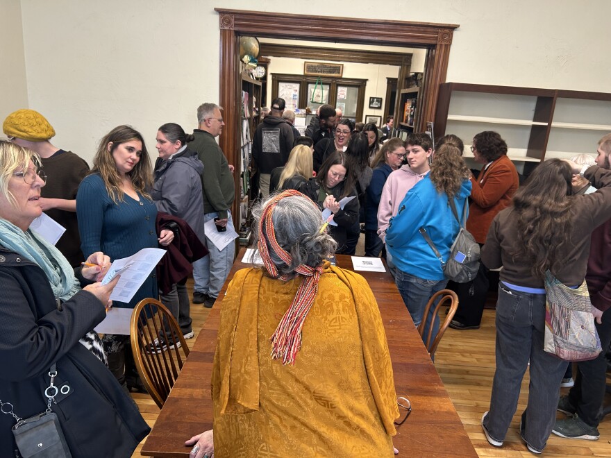 Leesa Guay-Timpson, in costume, with her back to the camera, speaks to the audience during the Memphremagog Community Theatre performance at the Haskell Free Library.