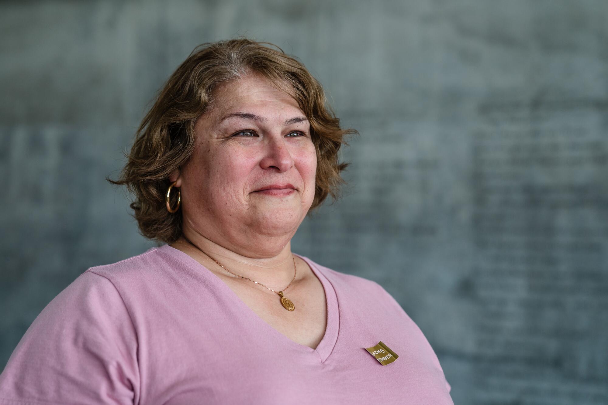 A woman in a pink shirt stands in front of a museum's concrete wall. 