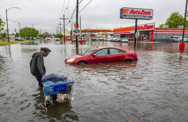 A person carries their belongings down a flooded street in New Orleans on April 10, 2024. (Chris Granger/The Times-Picayune/The New Orleans Advocate via AP)