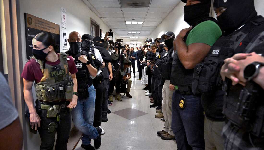 Masked federal officers wait outside courtrooms in New York City on July 8, 2025 holding target photographs.