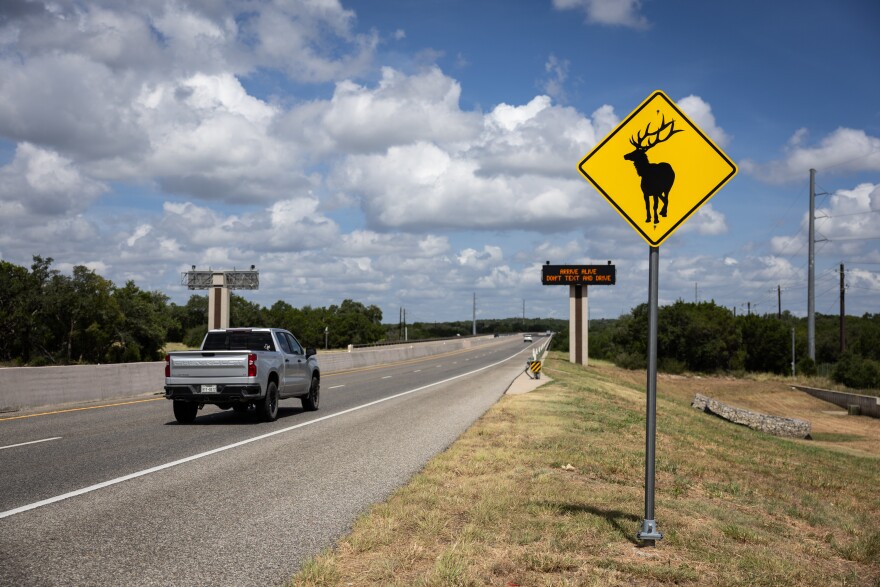 A photo of a yellow animal crossing road sign with an image of an elk stands by a highway.