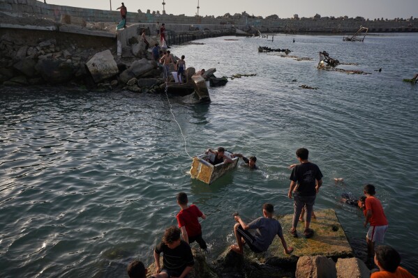 Palestinian youth play while swimming in a port basin in Gaza City, Sunday, April 19, 2026. (AP Photo/Jehad Alshrafi, File)