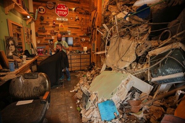 Barber Mohammad Mehdi cuts the hair of his client Ayman Al Zein inside his shop, which was damaged in an Israeli airstrike that also damaged Al Zein's shop, in Dahiyeh, Beirut's southern suburbs, Lebanon, Saturday, April 18, 2026. (AP Photo/Hassan Ammar, File)