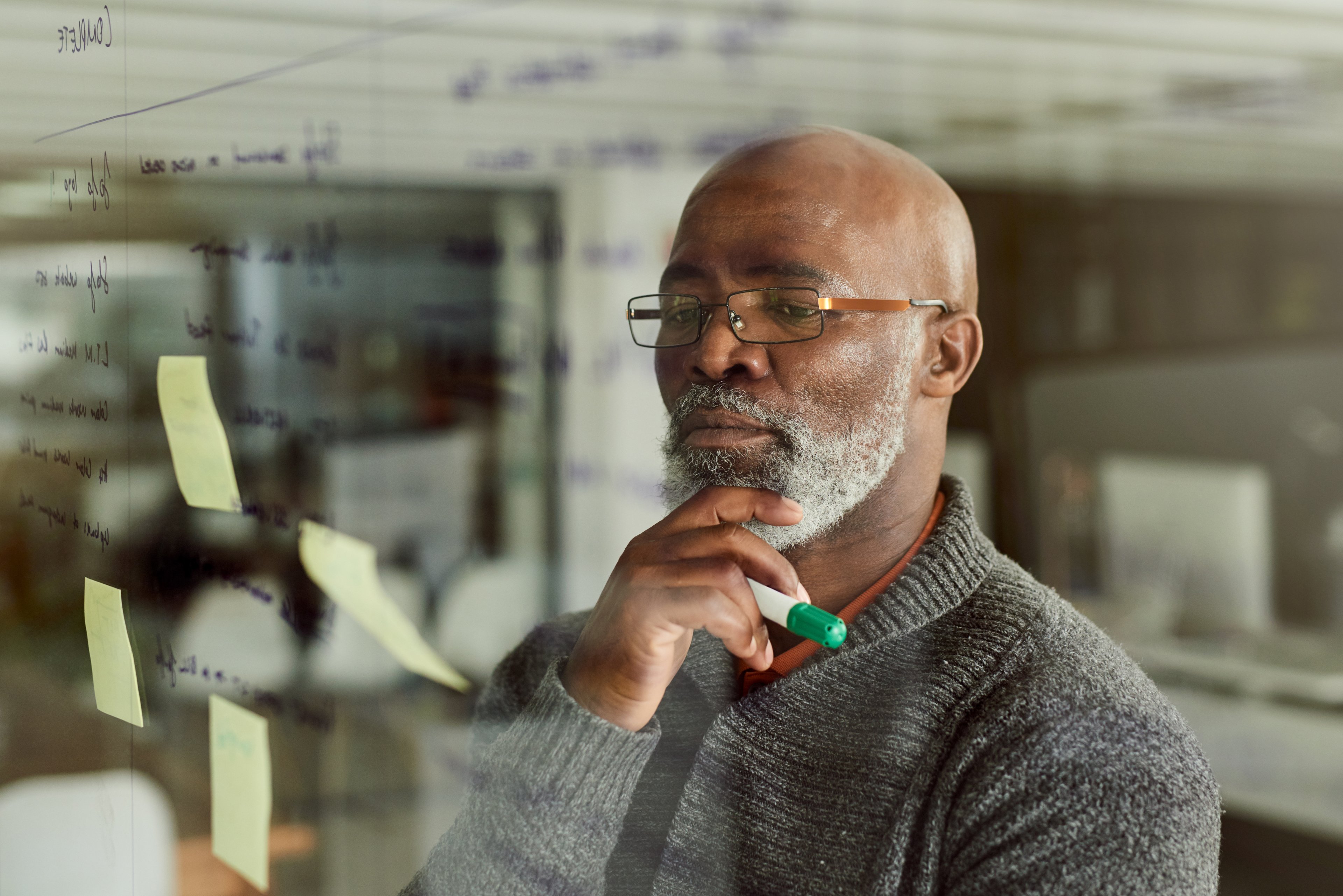 A person with hand on chin, holding a marker, thinking. 