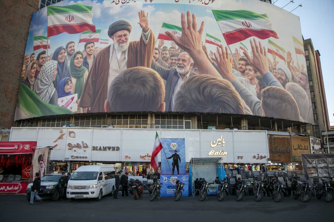 A police officer stands holding a flag in Valiasr Square beneath a mural of the late Ayatollah Ali Khamenei in Tehran, Iran, on Thursday.
