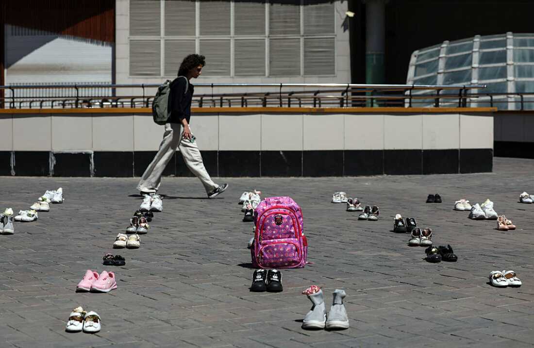 An Iranian woman walks past symbolic belongings laid on the ground at Valiasr Square in Tehran on April 24, 2026, in tribute to the schoolgirls in Minab killed in an airstrike.