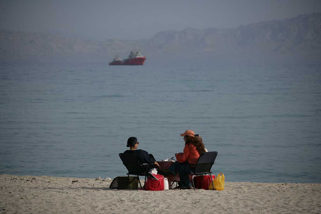 People sit on the beach with ships in the distance on April 24, 2026 in Kish Island, Iran.