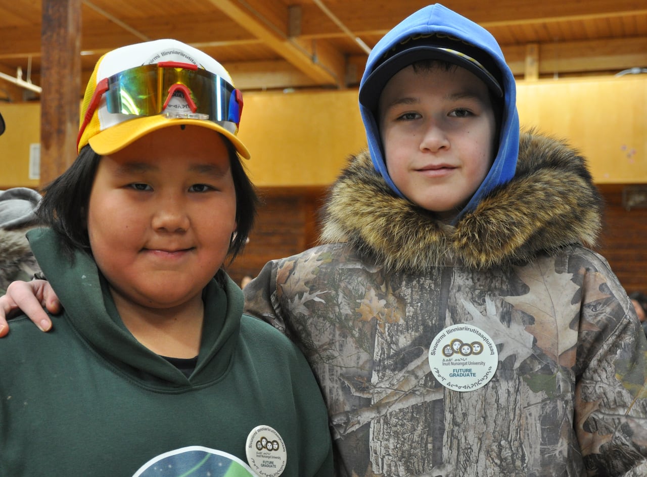 Two boys wearing caps are shown in a community hall.